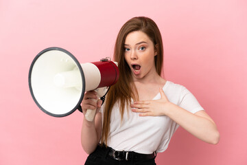 Teenager girl over isolated pink background shouting through a megaphone with surprised expression