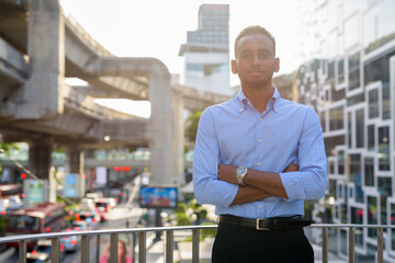 Portrait of handsome black African businessman outdoors in city during summer with arms crossed