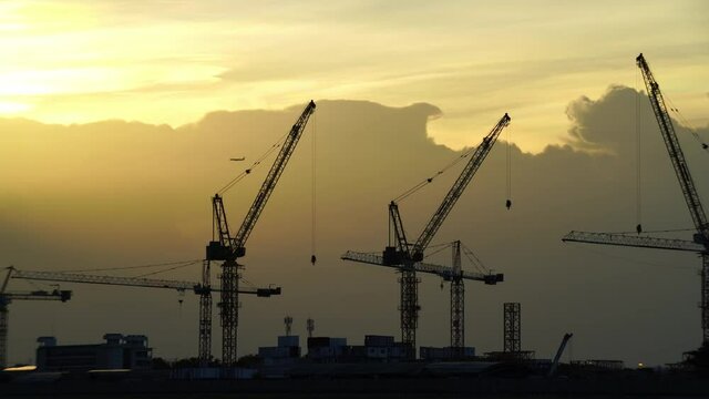 Cranes on the construction site or Big Container Cranes In The Port at sunset and the plane that slowly flew by._construction background