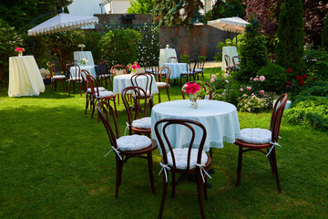 Fototapeta na wymiar Round table covered with white cloth and chairs stand on a green lawn outdoors.