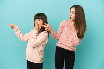 Little sisters girls isolated on blue background pointing finger to the side with a surprised face