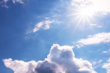 View of the blue sky with white cumulus clouds and the bright sun with rays and highlights