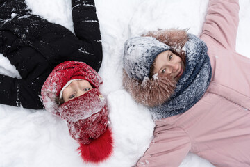 Teenage girls in snow-covered clothes lie in the snow and smile. People, lifestyle concept