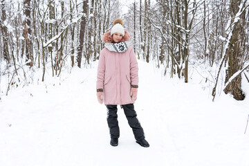 A teenage girl in a white hat and a pink jacket stands in a snowy forest and smiles. People, lifestyle concept