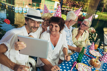 Senior people celebrating birthday in the cottage on the river having fun, make selfie photo.