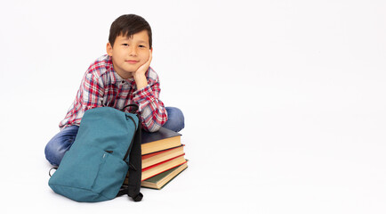 Young boy sitting with a pile of books and backpack on white