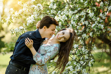  young beautiful couple  hugging and smiling in a blossoming cherry flowers tree.