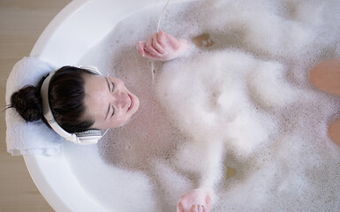 Happy young asian female with headphones singing in bathtub with eyes closed. Multi ethnic...