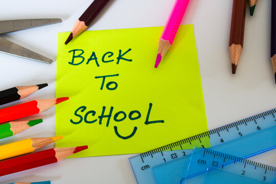 Back to school message on yellow sticky note with stationery scattered around isolated on white background