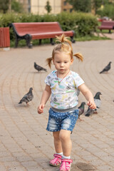 Little girl toddler runs after pigeons. Summertime