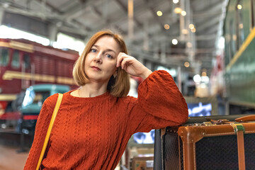 A young woman at the railway station at a trolley with suitcases
