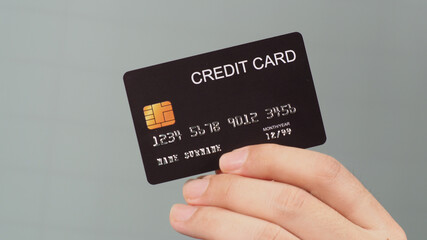 Hand is holding black credit card isolated on grey background.