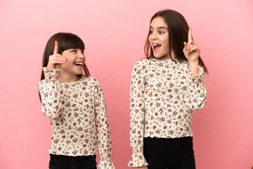 Little sisters girls isolated on pink background intending to realizes the solution while lifting a finger up