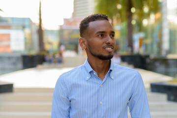 Portrait of handsome black African businessman outdoors in city during summer smiling and thinking