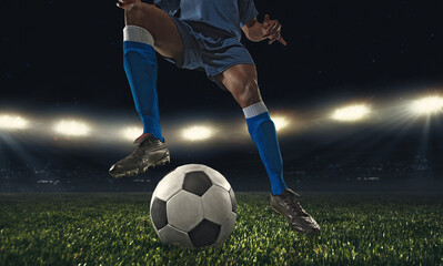 Cropped male soccer, football player kicking ball at the stadium during sport match on dark sky background.