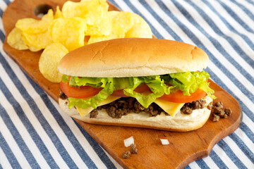 Homemade Chopped Beef Sandwich with Potato Chips on a rustic wooden board, side view. Close-up.