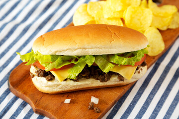Homemade Chopped Beef Sandwich with Potato Chips on a rustic wooden board, low angle view. Close-up.