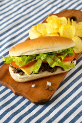 Homemade Chopped Beef Sandwich with Potato Chips on a rustic wooden board, side view.