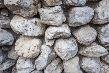 A close-up of a wall texture laid of stone boulders. Background pattern of grey color and different sizes and shapes. Backdrops, constructions, old ruins, travel.