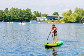 Kid boy paddling on sup board on a lake. Active child on modern trendy stand up paddle board....