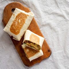 Homemade Breakfast Egg Burrito with Avocado and Bacon on a rustic wooden board, top view. Flat lay, overhead, from above. Space for text.