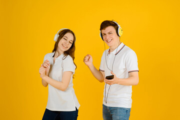 Portrait of a young happy couple man and woman listening to music in headphones and laughing on a yellow background.