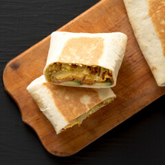 Homemade Breakfast Egg Burrito with Avocado and Bacon on a rustic wooden board on a black surface, top view. Flat lay, overhead, from above.