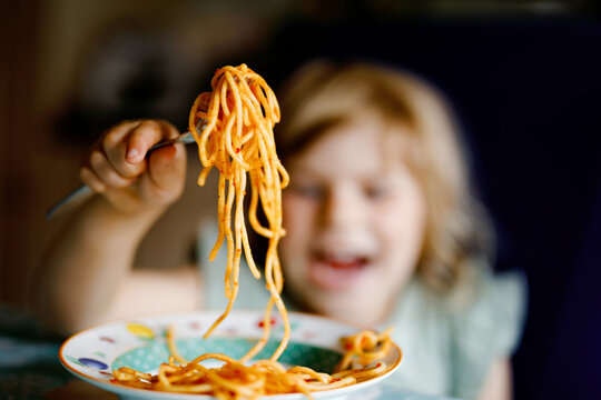 Adorable toddler girl eat pasta spaghetti with tomato bolognese with minced meat. Happy preschool child eating fresh cooked healthy meal with noodles and vegetables at home, indoors.