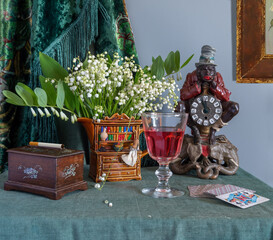 Still life with a glass of red wine, an antique clock, a bouquet of lilies of the valley and playing cards.