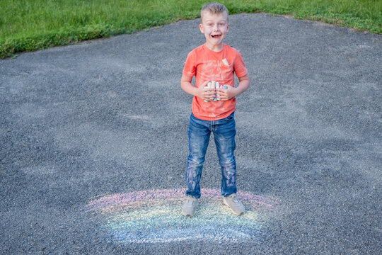 Surprised boy holding colored chalk in his hand, standing on a rainbow school playground.The concept of cleaning stains on clothes. 