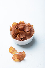 Cured meat in a white bowl, several meat chips on the background, vertical arrangement.