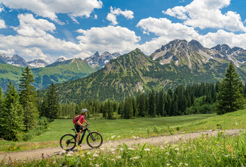 nice senior woman on mountain bike climbing up Mount Fellhorn in the Allgaeu High Alps with Trettach and Maedelegabel in background, Allgau, Bavaria, Germany