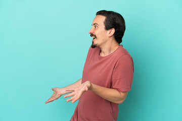 Young caucasian man isolated on blue background with surprise expression while looking side