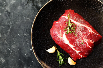 Raw beef steak with rosemary and garlic in a dark plate.