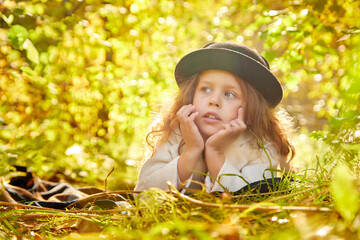 Portrait of young funny girl with blonde curly hair and in black hat in an autumn park on a yellow and orange leaf background
