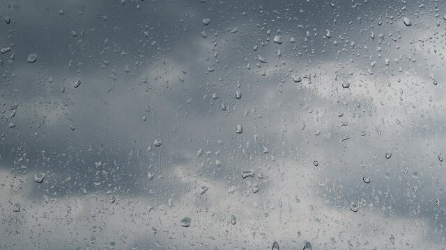 Raindrops roll down the glass against a cloudy sky.