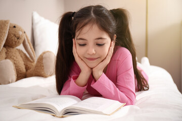 Little girl reading book on bed at home