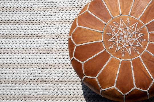 Boho style brown leather pouffe (ottoman) on a beige rug, copy space