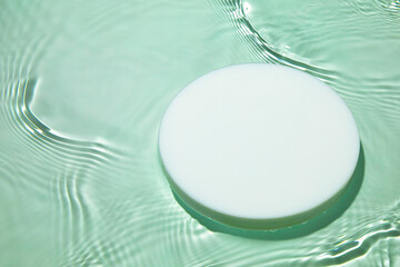 Empty white circle podium on transparent clear green calm water texture with splashes and waves in...