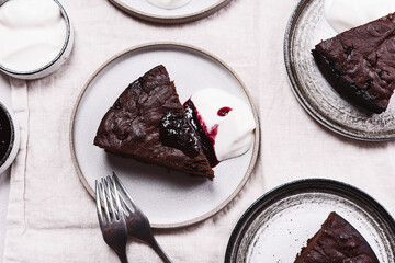 Slices of rich moist chocolate cherry cake. Homemade dark chocolate sweet brownies cakes with ice cream on greige linen tablecloth. Selective focus