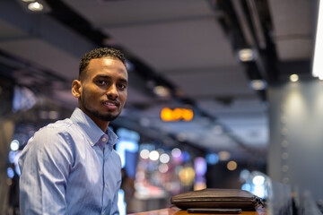 Portrait of handsome black African businessman sitting inside shopping mall