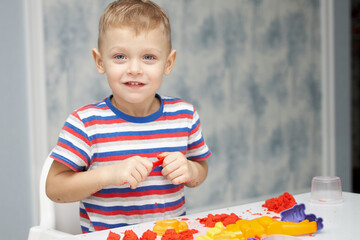 A cheerful little boy in a bright T-shirt plays with kinetic sand. Educational children's game with bright sand molds