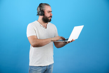 bearded man wearing headphones looks into a laptop on blue background. the concept of communicating with friends online via the internet