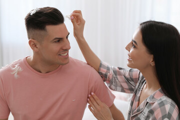 Happy woman taking off feather from boyfriend's head after pillow fight indoors