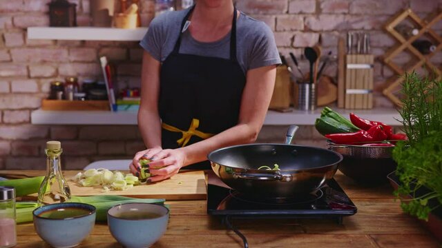 Woman cooking frying in wok pan on kitchen table.
