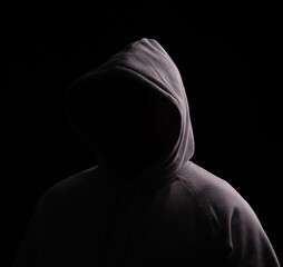 Hooded person with no face showing, just a dark area in that place, ideal for logo's and copy. Black background with moody lighting.