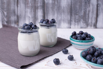 Greek yogurt in a glass jar and fresh blueberries on a rustic white table. Healthy food concept. Selective focus