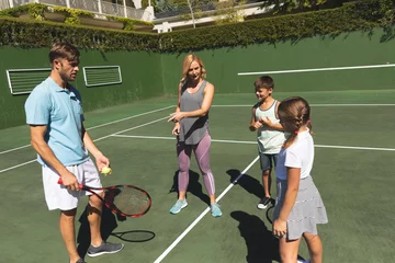 Wandaufkleber Happy caucasian couple with daughter and son outdoors, playing tennis on tennis court © wavebreak3