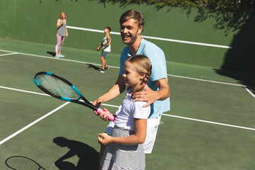 Happy caucasian couple with daughter and son outdoors, playing tennis on tennis court