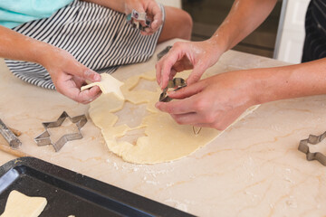 Caucasian mother and daughter baking together in kitchen, cutting cookies